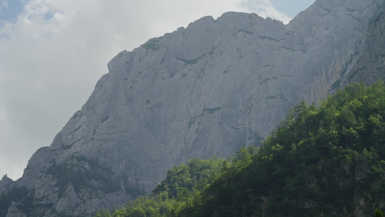 Rocky mountain peaks rise above lush green forests under a cloudy sky in Robanov Kot valley