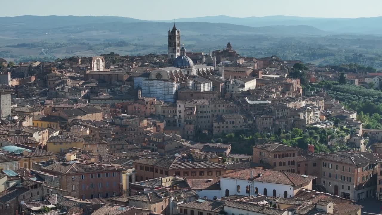 Ripresa statica con drone della fitta città medievale di Siena, in Italia, del Duomo e della circostante campagna toscana ondulata in una giornata limpida