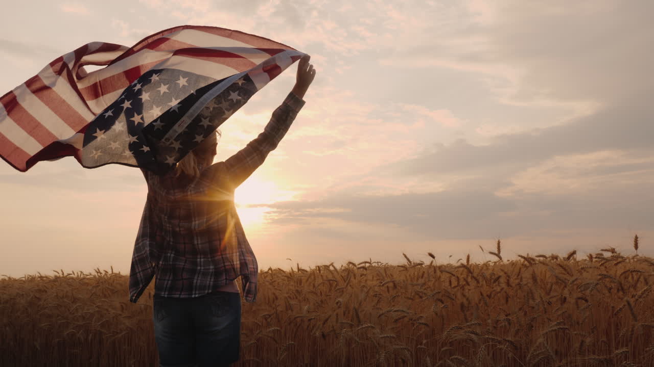 mujer con bandera de estados unidos corre bajo el sol en un campo de trigo