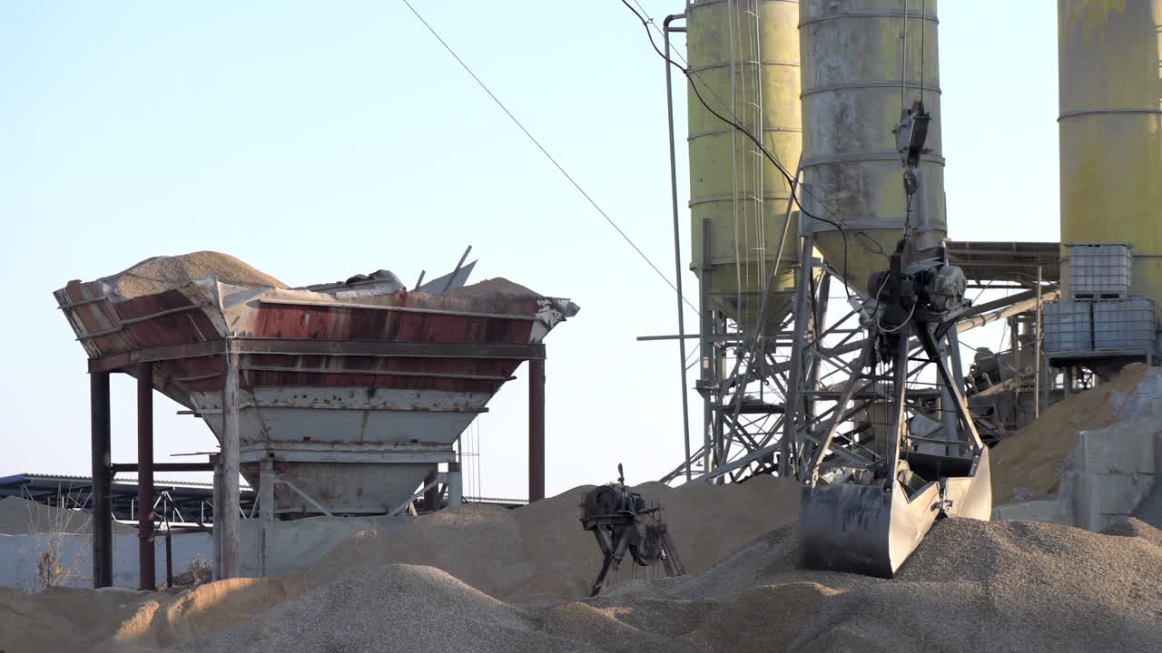 A mechanical grabber suspended by a crane loading and transporting piles of granular material on an industrial site