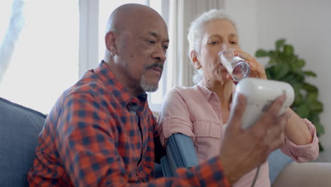 Serious-senior-biracial-couple-sitting-on-couch-and-taking-pressure-at-home,-slow-motion