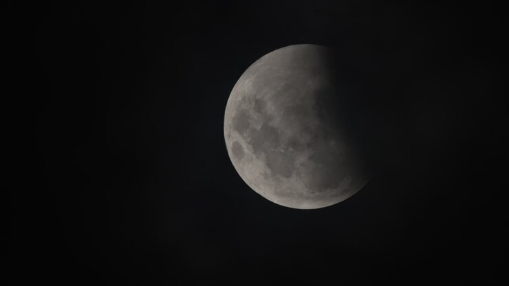 Close-up da lua no céu noturno durante um eclipse lunar, com o céu completamente escuro.