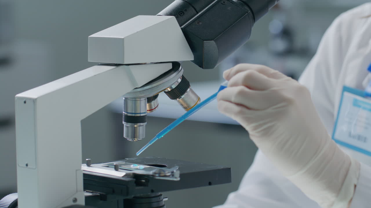Chemist Pouring Blue Liquid on Microscope Slide in Scientific Laboratory