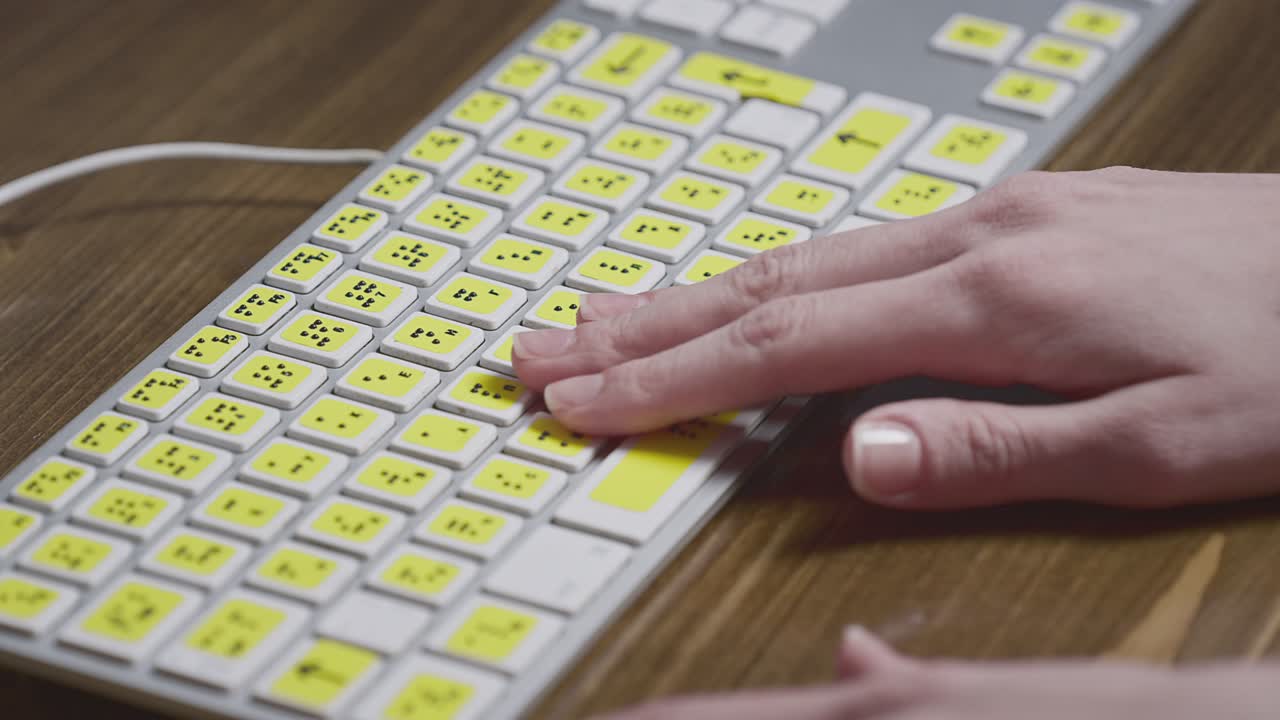 primer plano de un teclado de computadora con braille. una niña ciega está escribiendo palabras en los botones con sus manos.