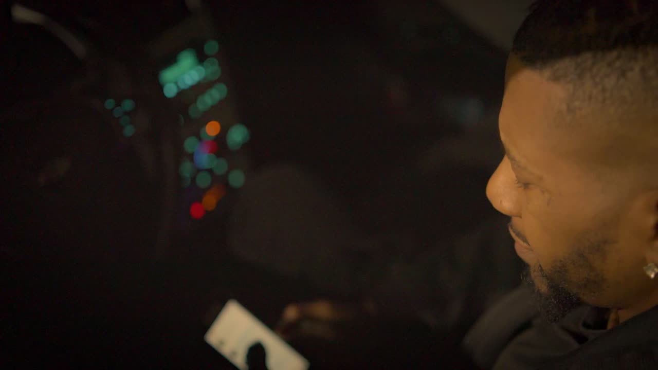 차의 운전석에 앉아 있는 흑인 남자가  ⁇ 드폰을 쳐다보고 있는 모습으로 분명히 괴로워하고 있습니다.