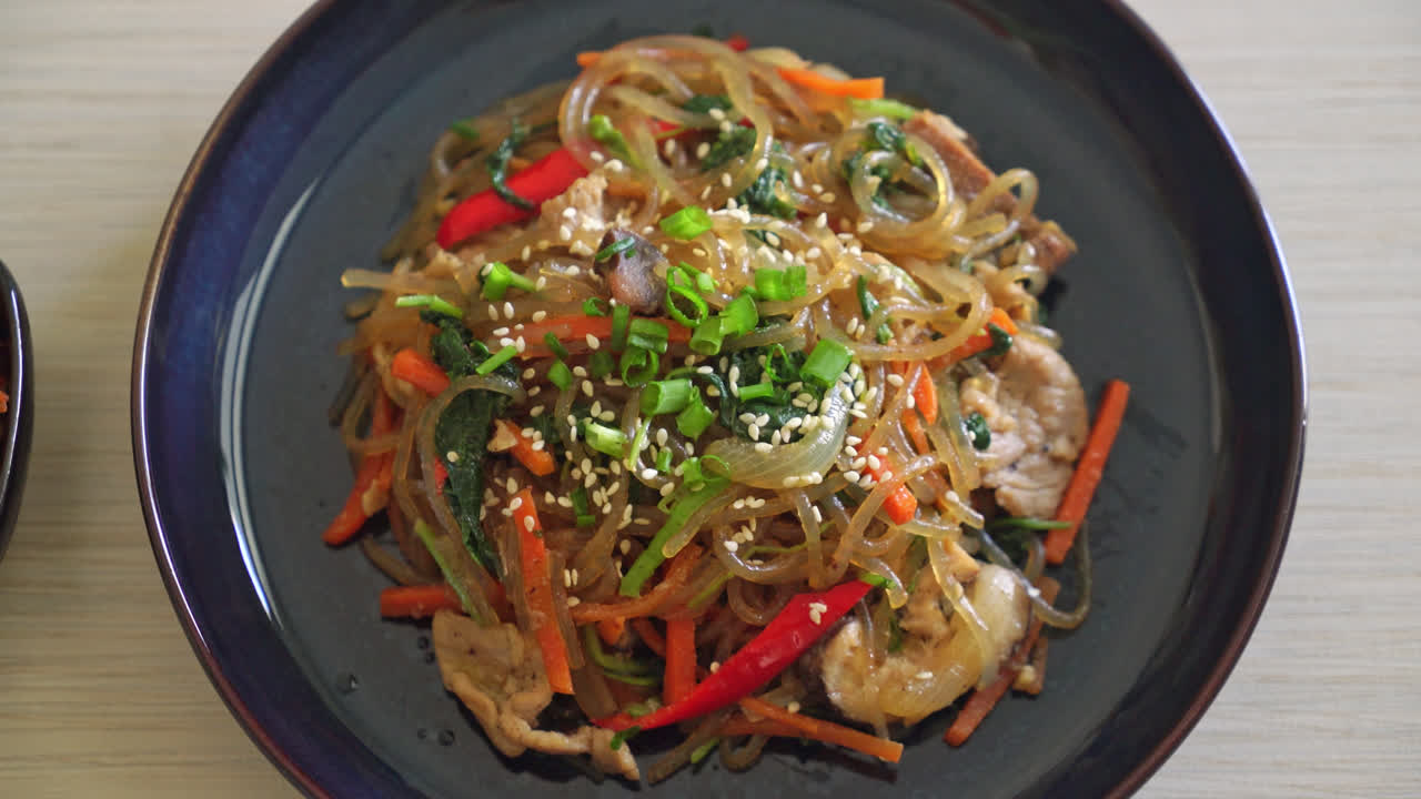 japchae o fideos vermicelli coreanos salteados con verduras y cerdo cubiertos con sésamo blanco - estilo de comida tradicional coreana