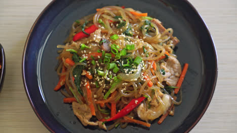 japchae or stir-fried korean vermicelli noodles with vegetables and pork topped with white sesame - korean traditional food style