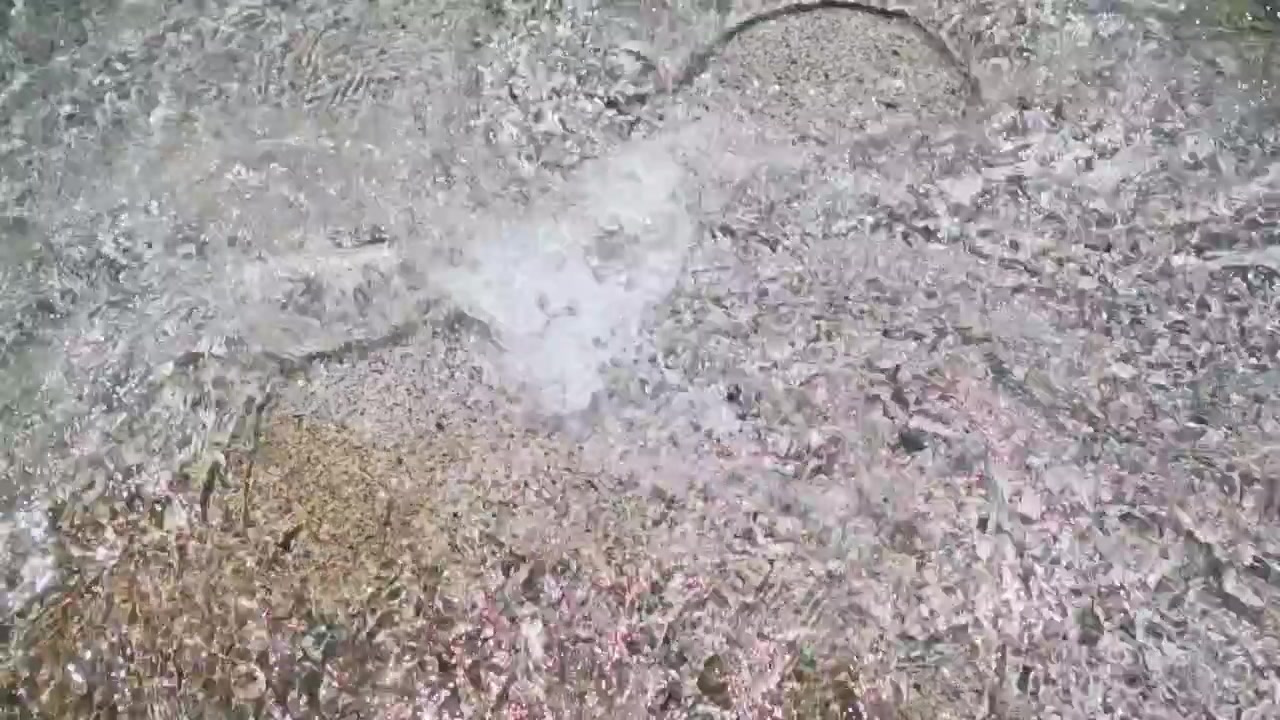 Agua clara y poco profunda fluyendo sobre un fondo arenoso con reflejos de luz solar.