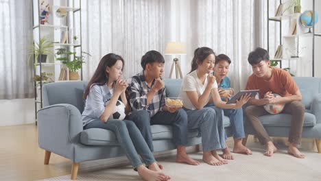 asian teenagers cheering and watching football game on tablet at home