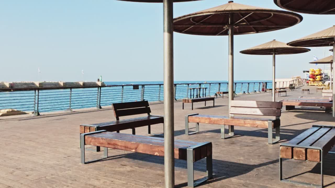 Puiset penkit ja aurinkovarjot Jaffa-sataman promenadilla merinäköalalla.