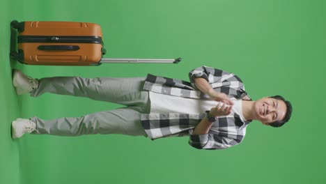 full body of asian male traveler with luggage smiling and clapping his hands while standing in the green screen background studio