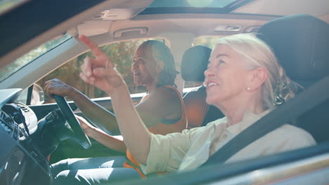 two senior female friends enjoying day trip out driving and sightseeing in car together