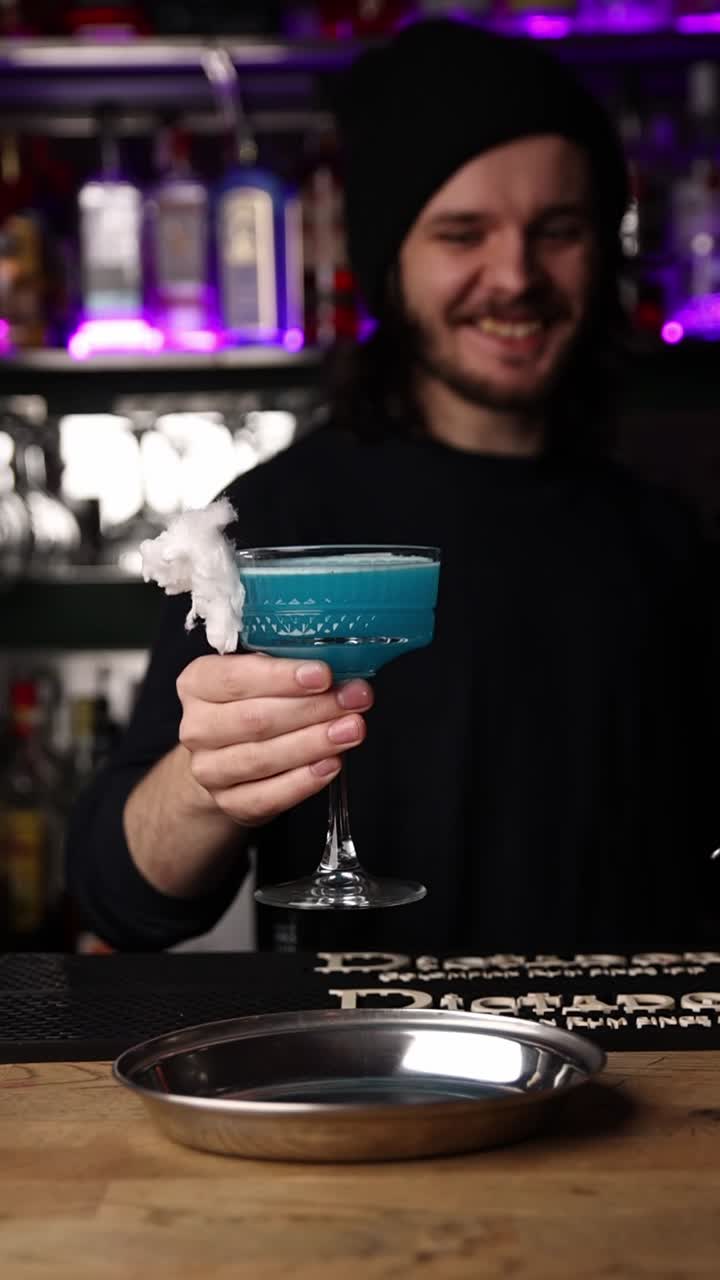 Un barman che tiene in mano un cocktail blu con zucchero filato