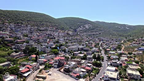 aerial view of the druze town of peki'in in northern israel, surrounded by lush green mountains under a clear summer sky.