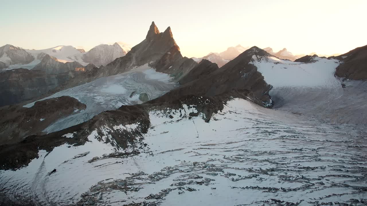 Aerial flyover over Glacier de Vouasson near Arolla in Valais, Switzerland with a golden sunset glow behind the Aiguilles Rouges, Mont Blanc de Cheillon, Grand Combin and other peaks