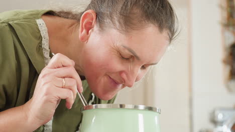 chef in green dress smiling warmly as she perceives aroma of cooking food with satisfaction while preparing meal in cozy kitchen, expressing happiness and pride through subtle
