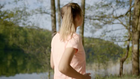 Woman-jogging-in-woods-next-to-lake-on-sunny-day