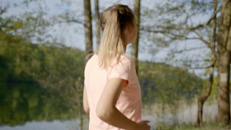 woman jogging in woods next to lake on sunny day