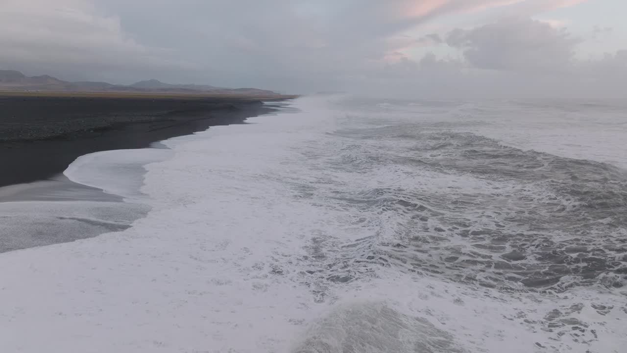 Aerial panoramic view of ocean waves crashing on Iceland S&oacute;lheimasandur black sand beach, on a moody day