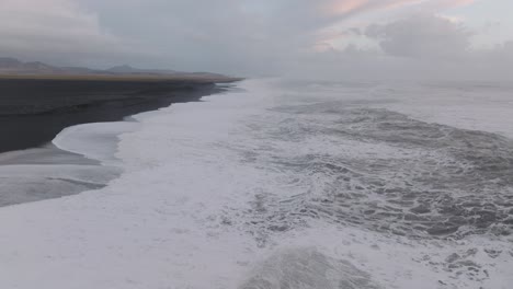 Aerial-panoramic-view-of-ocean-waves-crashing-on-Iceland-Sólheimasandur-black-sand-beach,-on-a-moody-day