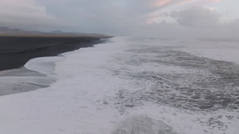 Luftpanorama-Der-Meereswellen,-Die-An-Einem-Launischen-Tag-Am-Schwarzen-Sandstrand-Von-Island-Sólheimasandur-Krachen