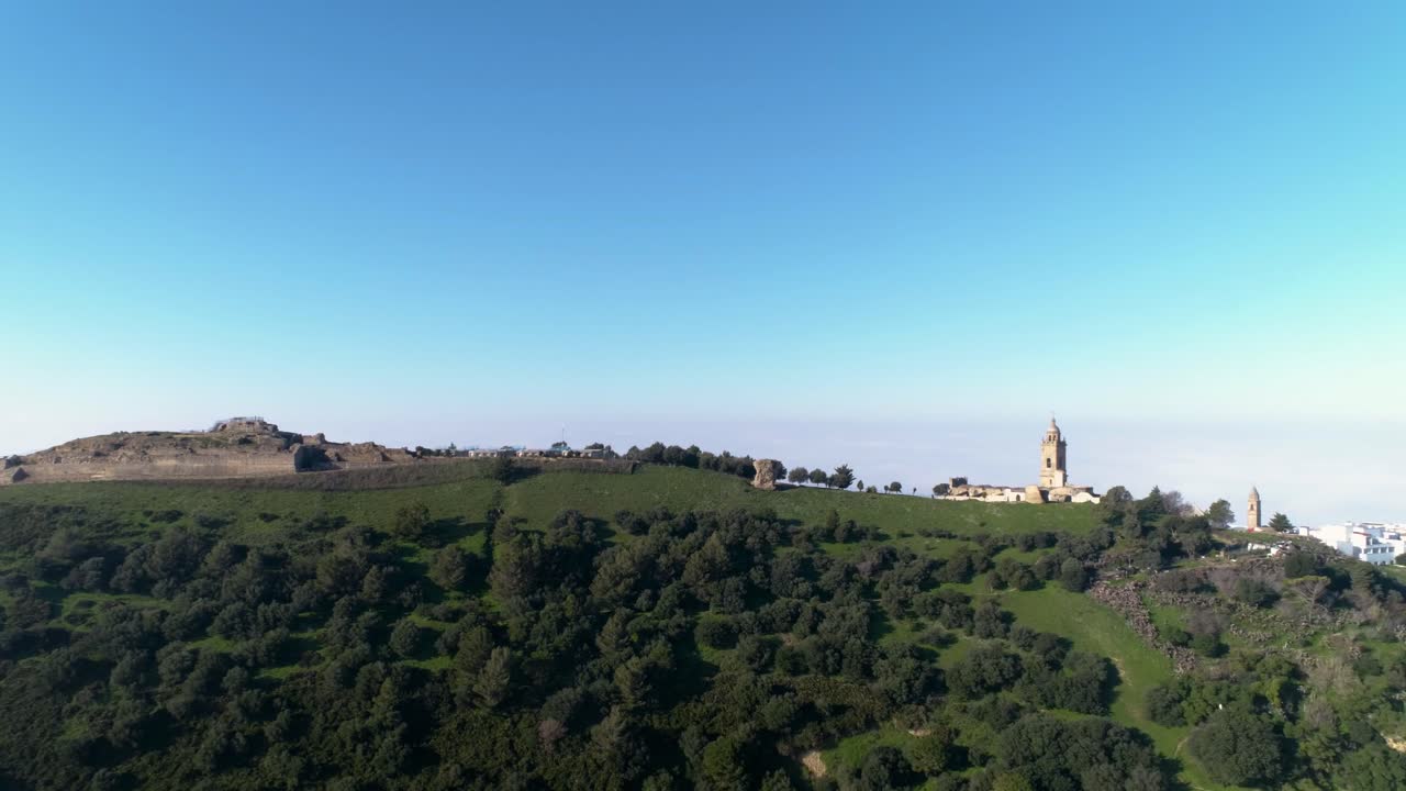 tiro aéreo desde una montaña en medina sidonia en la provincia de cádiz españa con vistas a las ruinas, la iglesia y los árboles en las colinas durante un día soleado