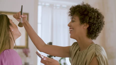 Side-view-of-young-Black-woman-applying-powder-on-friend's-face