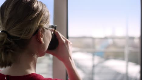 brown hair woman drinking cup while looking outside the city through window