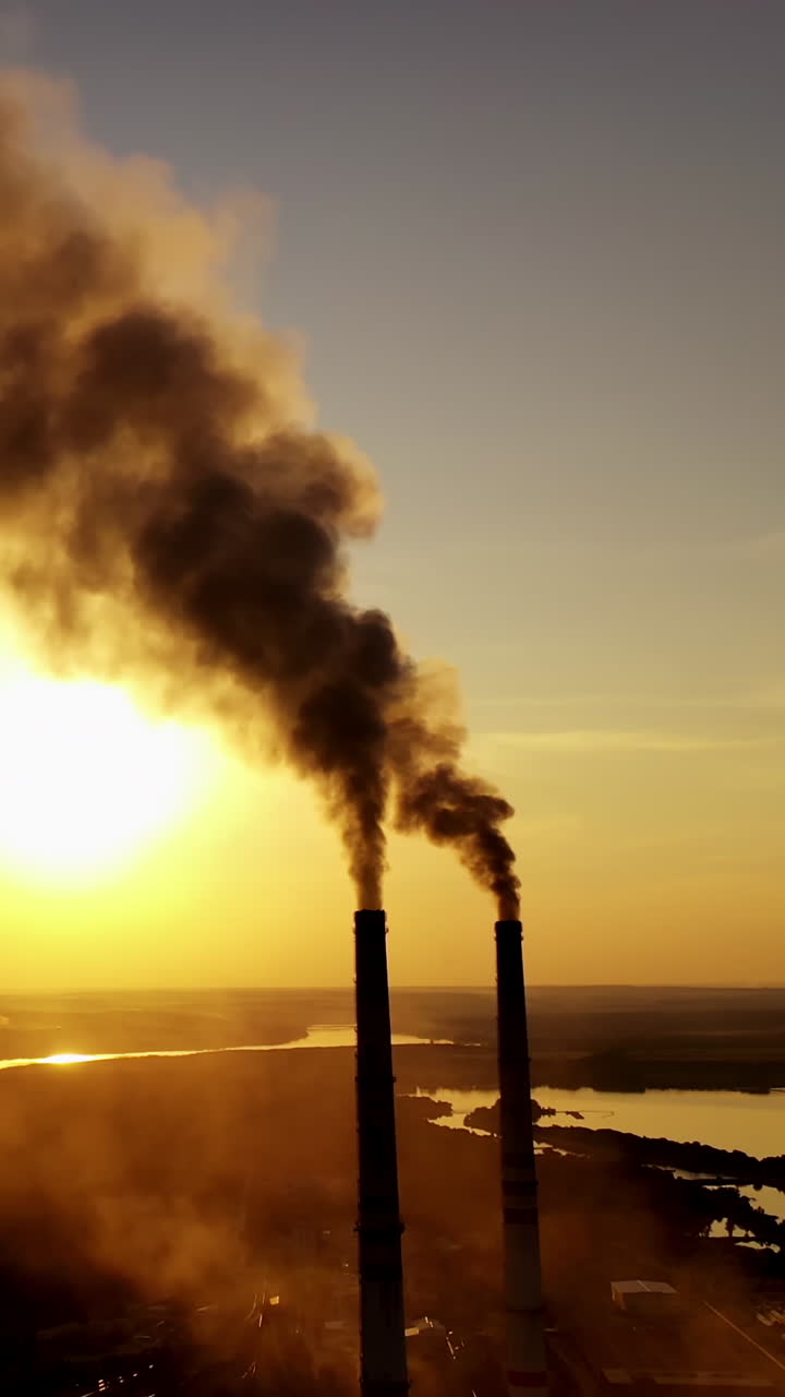 Dirty emissions in nature at sunset. Thick smoke coming from industrial pipes on the yellow sun setting background. Ecological disaster. Vertical video