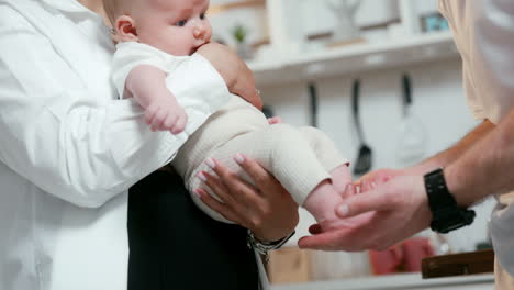 unrecognized caucasian parents with their newborn boy. mother holds the kid and father plays with tiny feet.