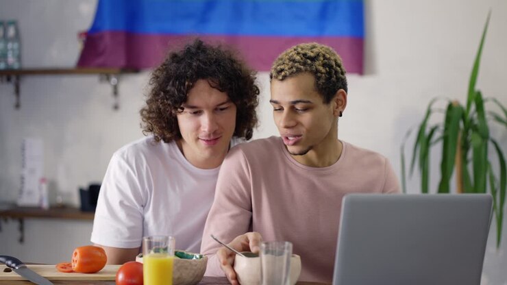 Pretty couple gay on the kitchen together during breakfast, watching news on laptop