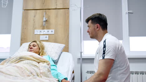 worried man talks to his pregnant wife lying in the bed. expecting couple in the maternity hospital ward. low angle view.