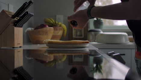 man sprinkles salt over dish on kitchen counter using hand mill