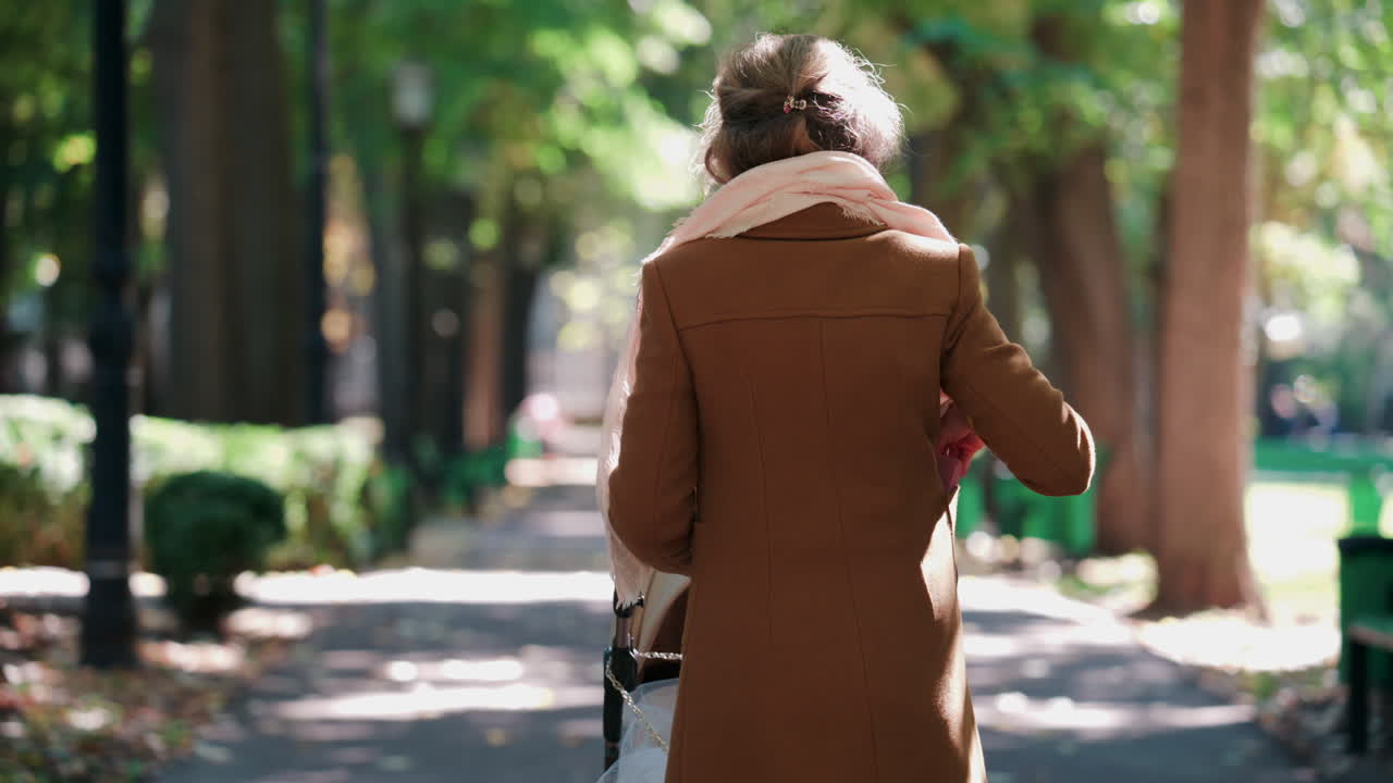 A woman pushing a baby stroller along a tree lined park path on an autumn day