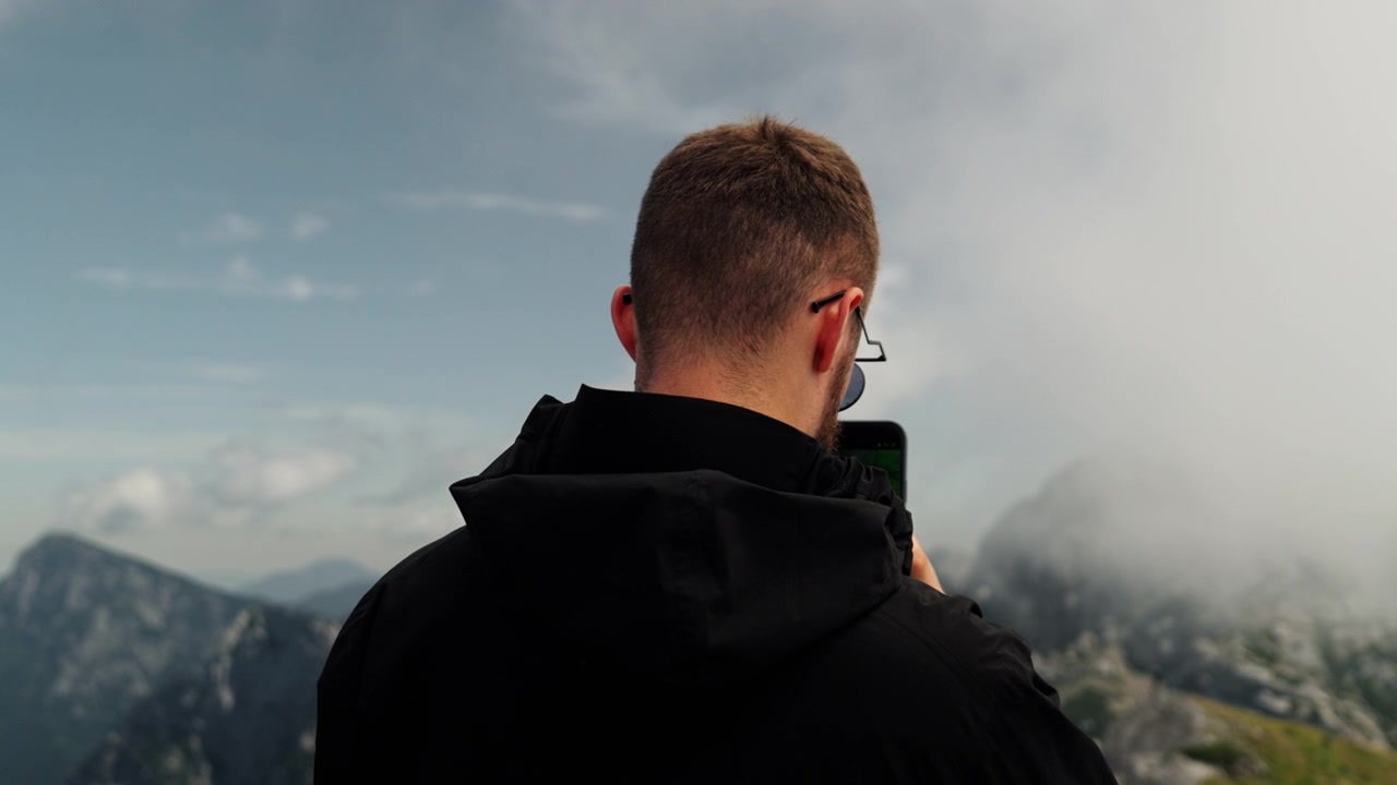 Uomo usa uno smartphone per registrare un paesaggio montano durante un'escursione all'aperto. Momento di viaggio panoramico che mostra riprese mobili, avventura ed esplorazione della natura.