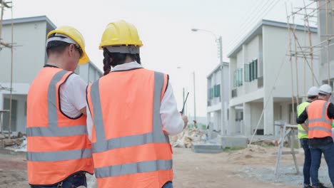 vista trasera de la mujer asiática ingeniera civil o arquitecta, inspector con contratista, capataz o trabajador usan casco de seguridad. colegas discutiendo, reuniéndose sobre el proyecto de construcción en el sitio.