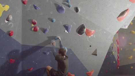 low angle shot of a strong male athlete climbing artificial rock wall in bouldering gym 1