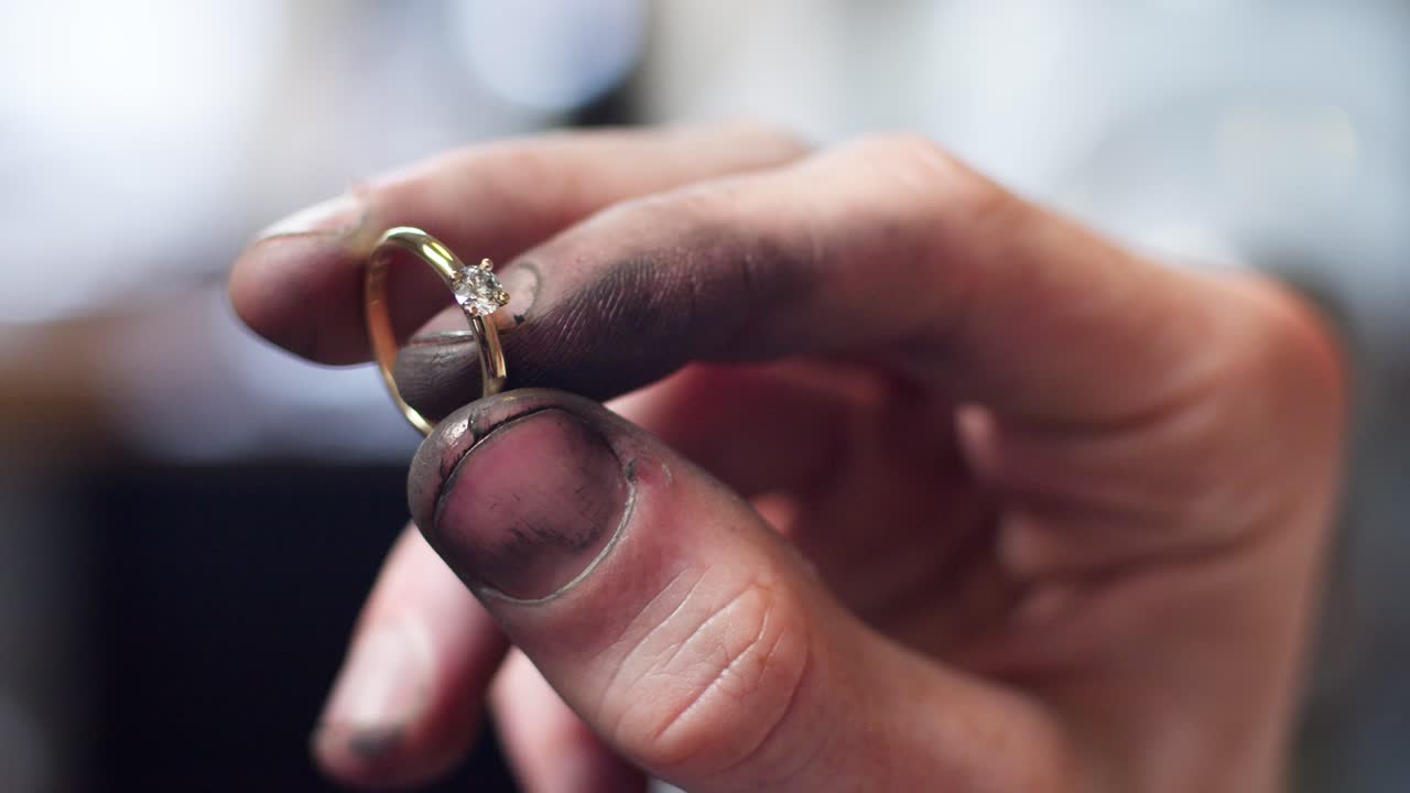 Closeup of a diamond wedding ring and dirty jeweller hands holding it