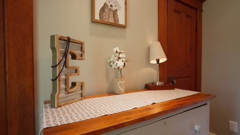 orbiting shot of a dresser decorated with a large letter e and small vase and a small light