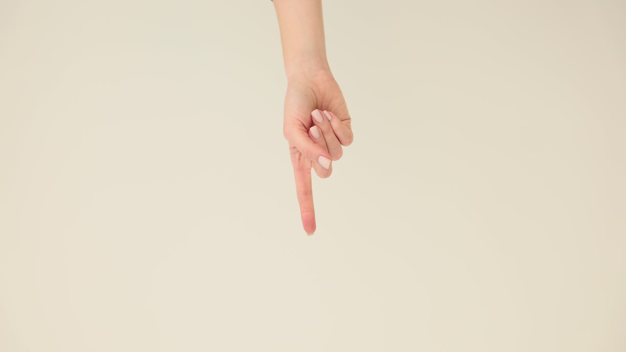 A close-up of a human hand pointing downwards with the index finger on a light background