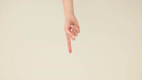 a close-up of a human hand pointing downwards with the index finger on a light background