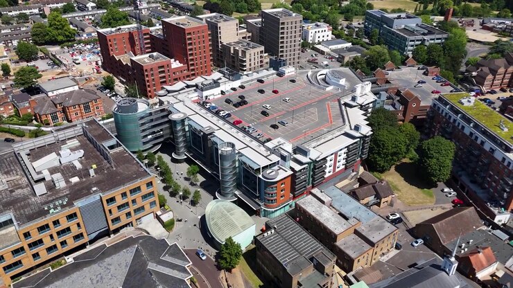 Office building with a rooftop car park and circular glass stair towers stands among the mixed rooftops of a town centre