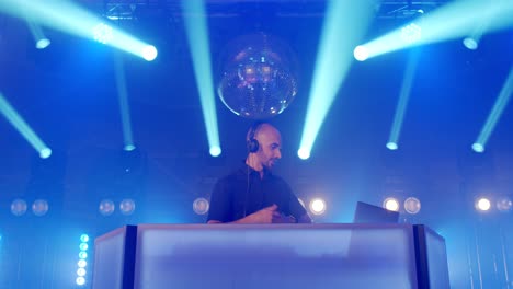 live dj performance of energetic bald man with headphones, dancing on party concert musician stage