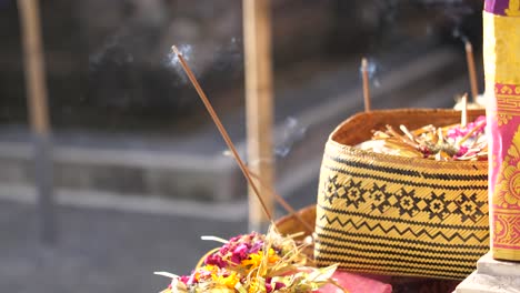 baskets filled with flowers for hindu religious offerings with burning sticks of incense at temple in bali