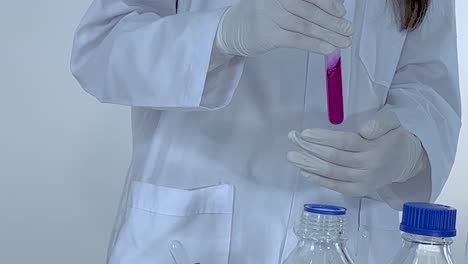 A scientist in a lab coat holds a pink liquid-filled test tube over a beaker.