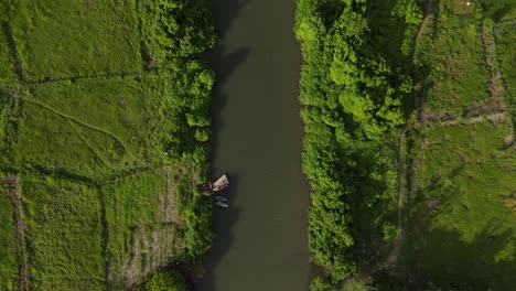 aerial view, canoe leaning on the river bank with thick green trees on the river bank