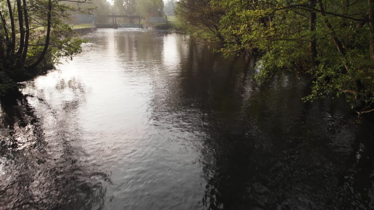 Drone clip over the running water of a small river with a bridge in the background in the countryside of Thetford in England