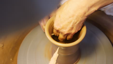 close up of male potter shaping clay for pot on pottery wheel in ceramics studio