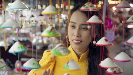 close up of young vietnamese tourist in yellow dress touching souvenirs in hoi an, vietnam