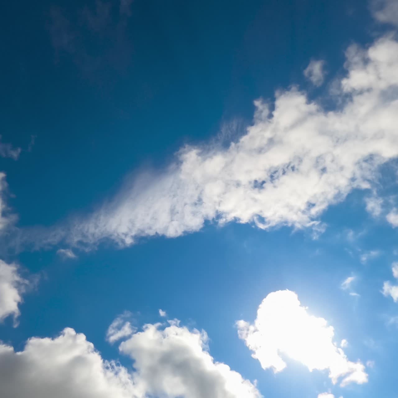 White cotton clouds quickly flying in the sky. Heavy clouds at the backdrop of blue and sunny skies. View from below